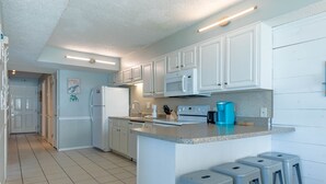 A modern kitchen with white cabinets, a central island with stools, a microwave, and a toaster. - Summit 2BR 2BA 13th Floor End Unit w/ BEACH CHAIRS INCL!!! (Panama City Beach)