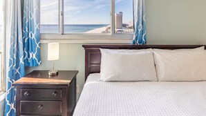 A hotel room with a bed, a nightstand, a lamp, and a window with a view of the beach and ocean. - Summit 2BR 2BA 13th Floor End Unit w/ BEACH CHAIRS INCL!!! (Panama City Beach)