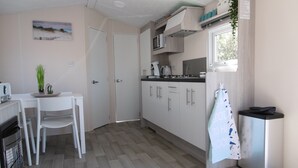 Uma cozinha compacta com armários brancos, micro-ondas e pia. Há uma área de refeições com mesa e cadeiras, e uma pequena planta em vaso.