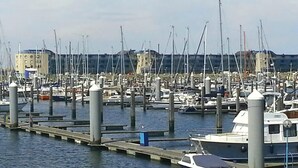 Marina com vários barcos atracados em cais, um canal e edifícios ao fundo.