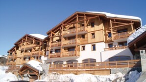 Un chalet en bois à plusieurs étages, doté de balcons, situé dans un paysage enneigé.