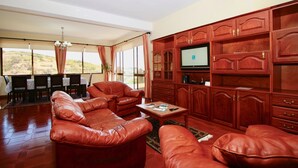 A spacious living room with leather sofas, a wooden entertainment unit, and a dining area with a view. - Villas Quinta da Lapa 2. Villa. Heated pool. WiFi (Câmara de Lobos)
