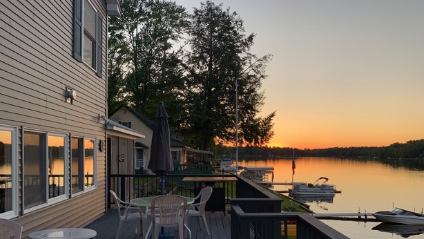 Une terrasse en bois avec des meubles d’extérieur, une vue sur un lac et des bateaux amarrés.