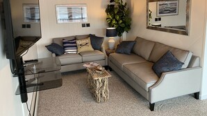 Un salon avec un canapé, une table basse, un téléviseur et une plante.