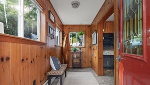 Un couloir en bois avec un banc, une petite table sur laquelle est posée une plante, et une porte rouge.