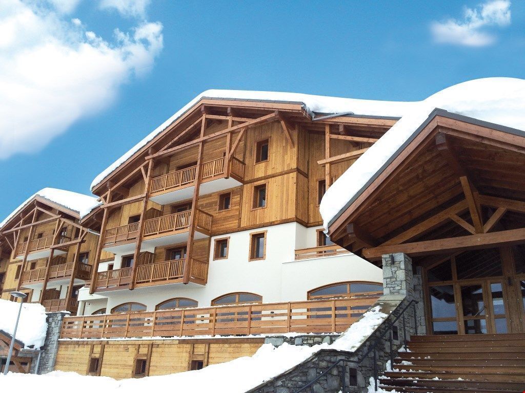 A multi-story wooden building with balconies, stone steps, and snow accumulation.