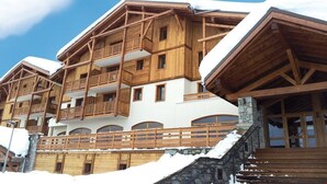 Un immeuble en bois à plusieurs étages, doté de balcons, d’escaliers en pierre et recouvert de neige.