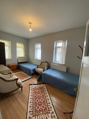 A bedroom with two single beds, a wooden floor, a patterned rug, a chair, and a radiator. - Acan Apart Pansiyon (Ürgüp)