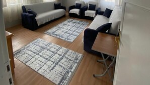 A spacious living room with a sofa set, two rugs, and a wooden floor.