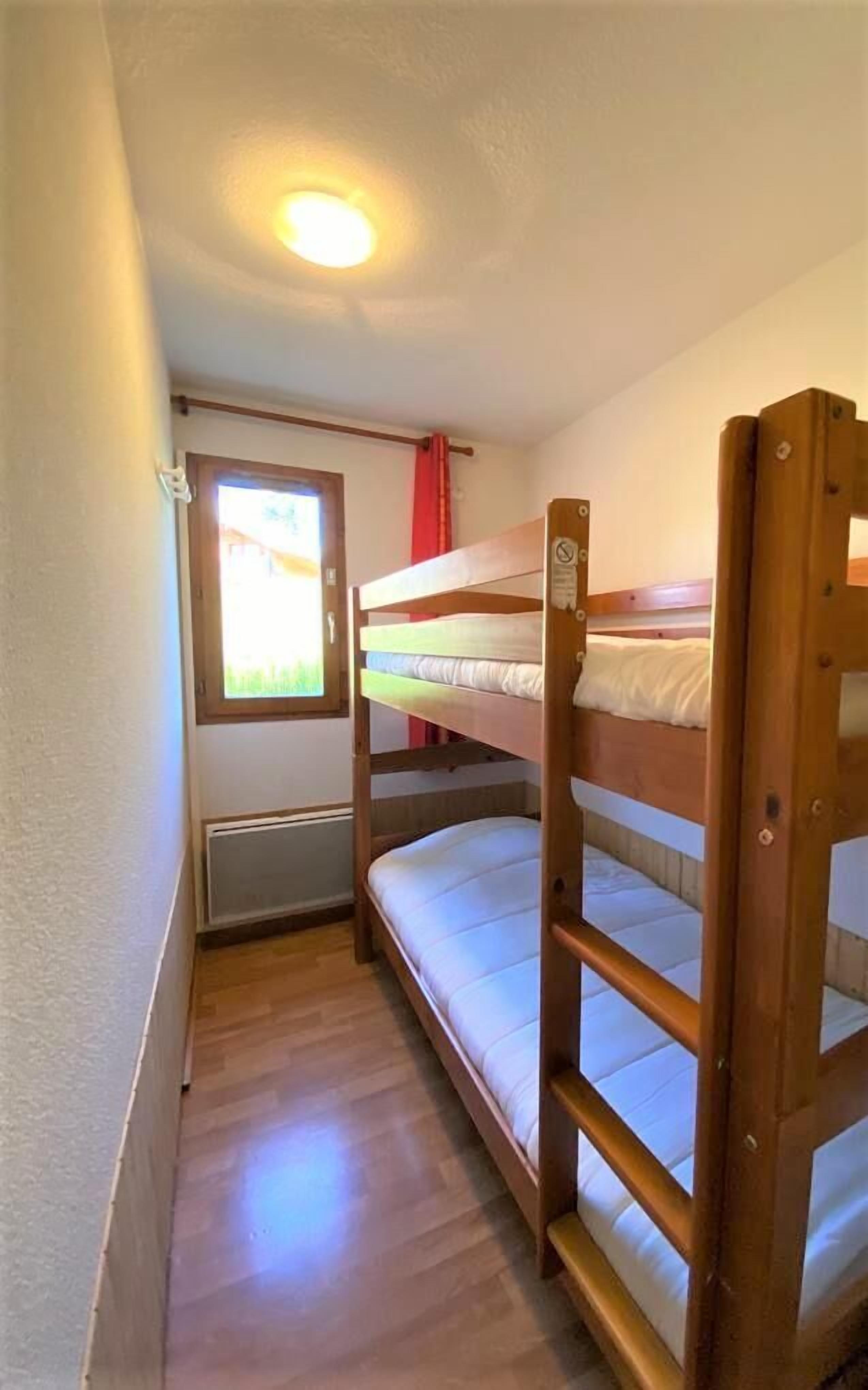 Una habitación pequeña con literas, una ventana y vistas, y un radiador.