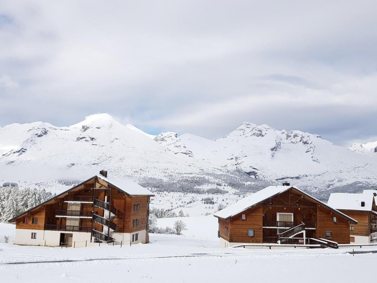 Two wooden cabins with balconies, set against a snowy mountain backdrop.