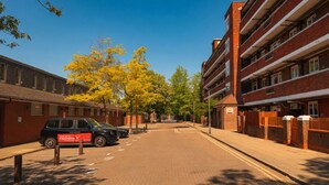 Een straat met een geparkeerde auto, een rood bord en een meerlaags gebouw met een bakstenen gevel.