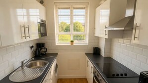 Een moderne keuken met witte kastjes, een zwart aanrecht, een ingebouwde magnetron en een raam met jaloezieën.