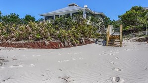 A beachfront property with a house, a wooden staircase leading to a deck, and a sandy beach. - Old Florida, View of St Vincent's Island, Near Boat Landing ~ Island Idyl (Indian Pass)
