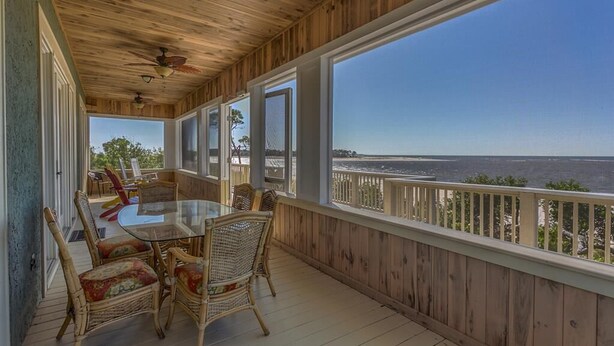 A wooden deck with a glass table and wicker chairs, overlooking a body of water. - Old Florida, View of St Vincent's Island, Near Boat Landing ~ Island Idyl (Indian Pass)