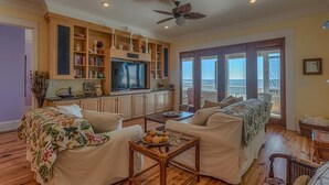 A spacious living room with a large TV, wooden cabinets, and a balcony with a view. - Old Florida, View of St Vincent's Island, Near Boat Landing ~ Island Idyl (Indian Pass)