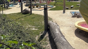 Un terrain de jeux avec des toboggans et des structures d’escalade, entouré d’arbres et sous un ciel dégagé.