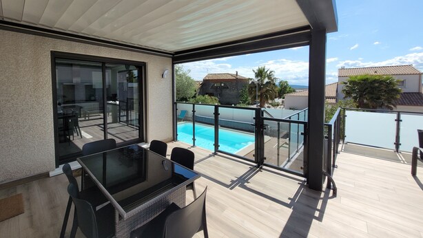 Une terrasse extérieure moderne, dotée d’une table et de chaises en verre, d’une piscine et offrant une vue sur les maisons voisines.