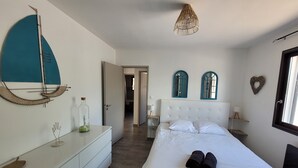 Une chambre à coucher comprenant un lit, des tables de chevet, une commode, un luminaire suspendu et deux fenêtres en arc de cercle.