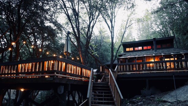 A wooden deck with stairs leading to a building with windows. - NEW: Elegant creekside cabin with waterfall (Idyllwild-Pine Cove)