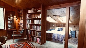 A cozy attic bedroom with a sloped ceiling, a large bookshelf, a desk with a chair, and a bed with a patterned bedspread. - NEW: Elegant creekside cabin with waterfall (Idyllwild-Pine Cove)