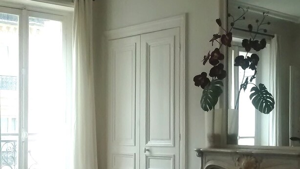 Un salon doté d’un lustre moderne, d’une cheminée, d’un grand miroir et offrant une vue sur l’extérieur par une fenêtre.