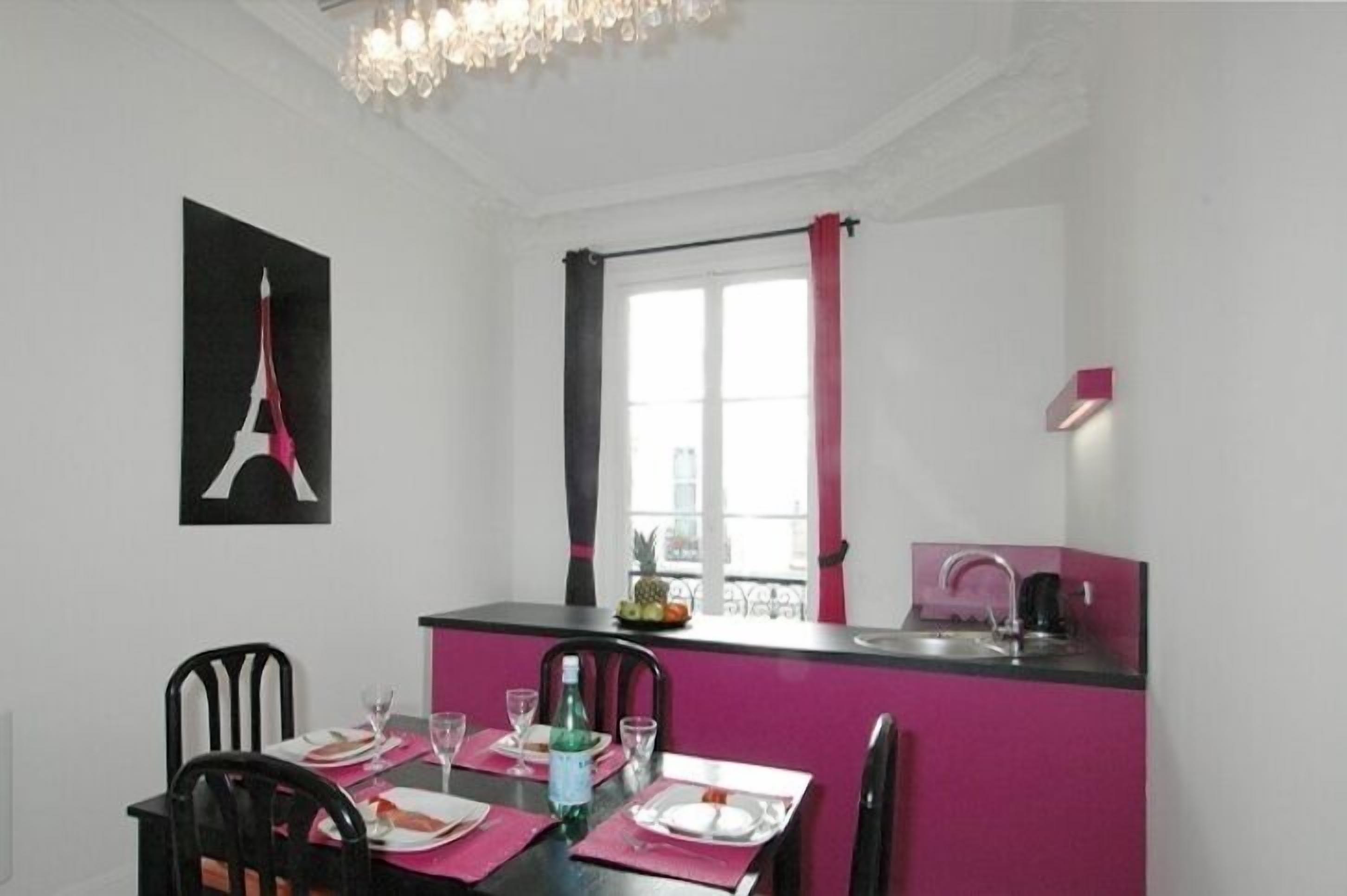 A dining area with a table set for four, a kitchen counter with a sink, and a window with curtains.