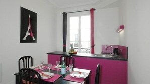 Un coin repas avec une table dressée pour quatre personnes, un plan de travail de cuisine avec un évier et une fenêtre avec des rideaux.
