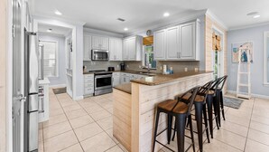 A modern kitchen with white cabinets, a central island with stools, and a built-in microwave. - Two Golf Carts ~ Private Pool ~ Screened Porch (Miramar Beach)