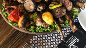 Una mesa con diversos cortes de carne a la parrilla, verduras y un vaso de bebida verde.