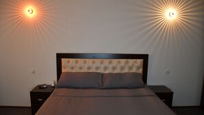 Un dormitorio con cabecera capitonada, dos mesitas de noche y dos lámparas de pared.
