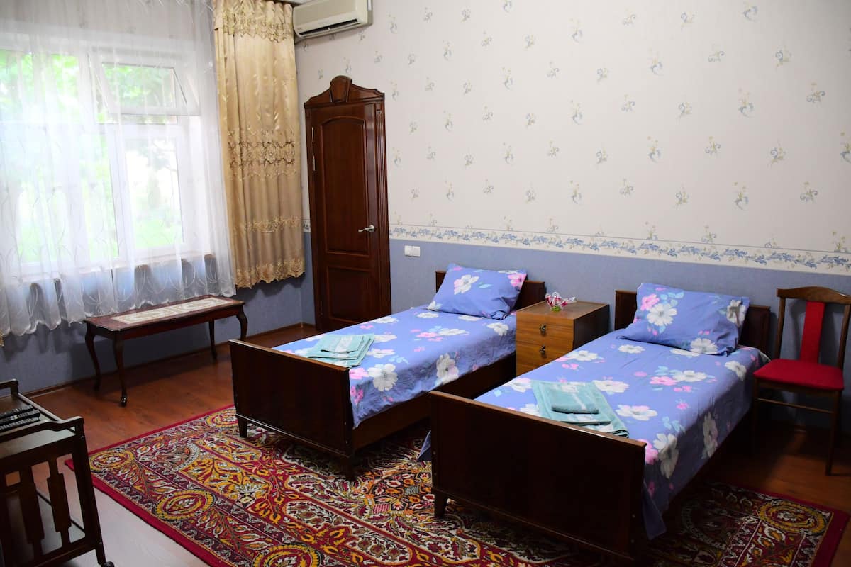 A bedroom with two single beds, a wooden wardrobe, a bench, and a patterned rug.