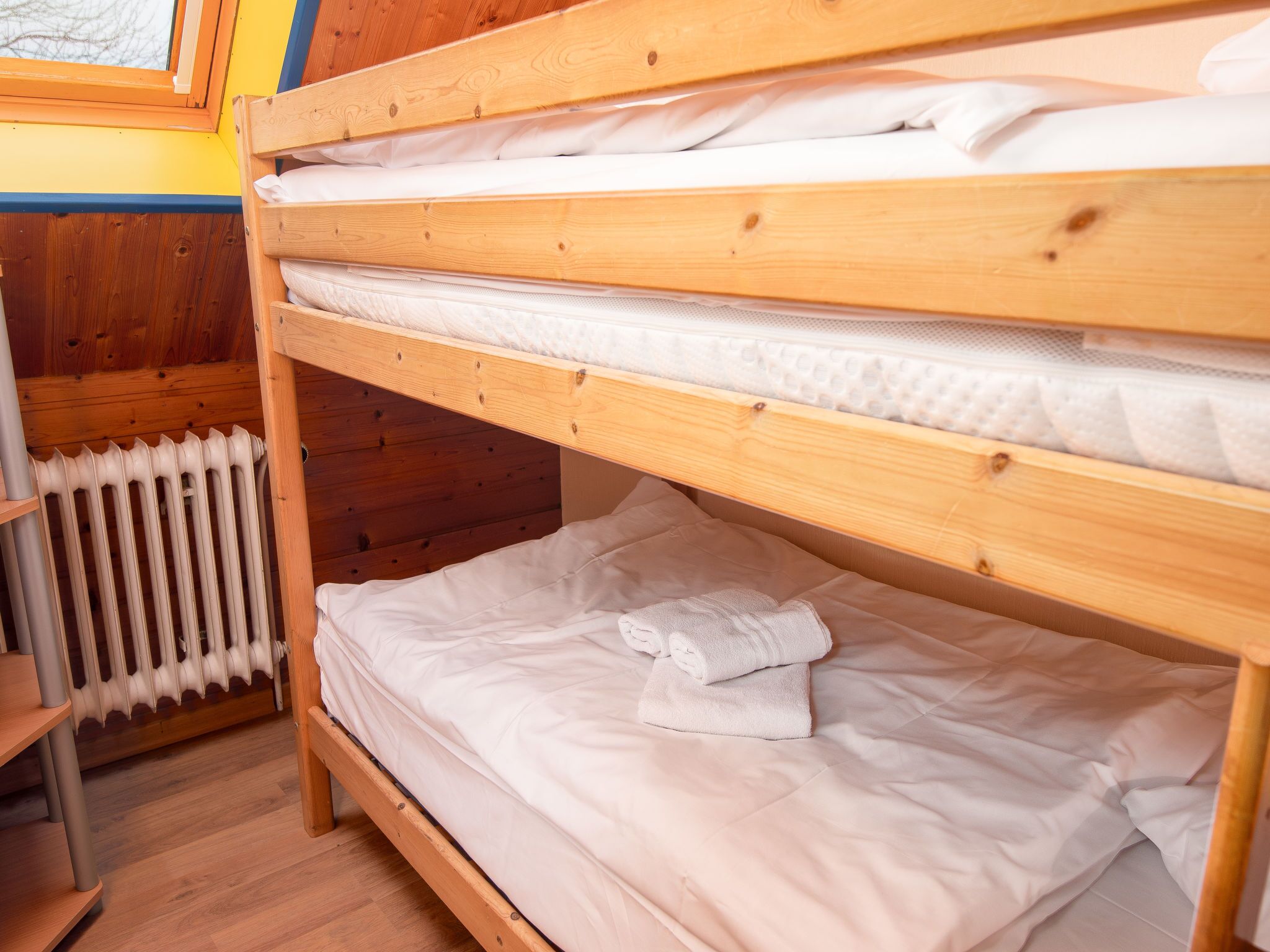 Una cama litera con ropa de cama blanca y una toalla enrollada.