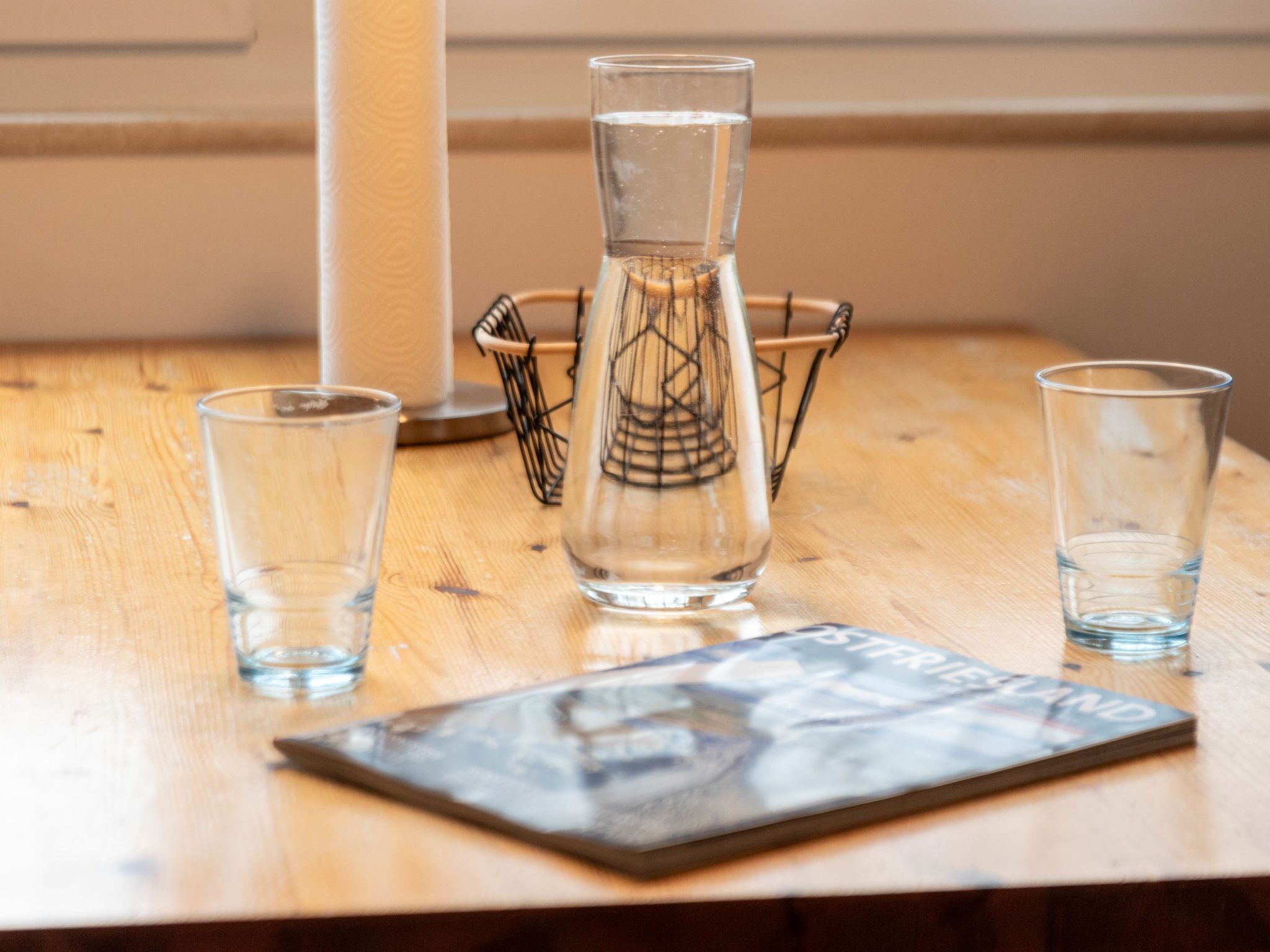 A wooden table with three clear glasses, a decorative glass pitcher, and a magazine.