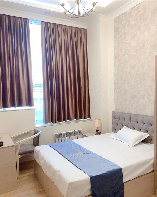 Habitación de hotel con cama, escritorio, silla, radiador y ventana con cortinas.