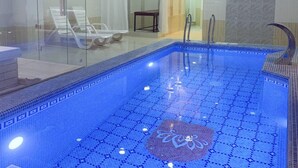 Ein moderner, überdachter Pool mit großen Glaswänden, gefliestem Boden und einer Lounge mit Stühlen und Tisch.