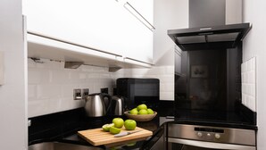 Eine moderne Küche mit Backofen, Mikrowelle und Wasserkocher. Auf einem Schneidebrett liegen Äpfel, und eine Schüssel mit Äpfeln steht auf der Arbeitsfläche.