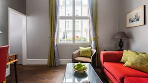 Ein Wohnzimmer mit Glastisch, rotem Sofa, braunem Sessel und einem Fenster mit Vorhängen.