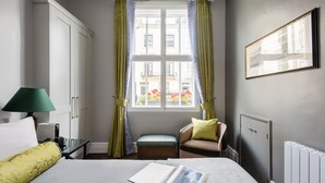 Ein Hotelzimmer mit einem Bett, einem Vorhangfenster, einem Sessel, einer Lampe und einer Heizung.