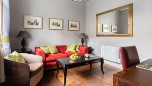 Ein Wohnzimmer mit einem roten Sofa, einem beigen Sessel, einem schwarzen Couchtisch mit einer Schüssel Äpfeln und einem großen Spiegel an der Wand.