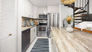 Cuina moderna amb armaris blancs, electrodomèstics d'acer inoxidable, taulell de marbre i una escala espirala.