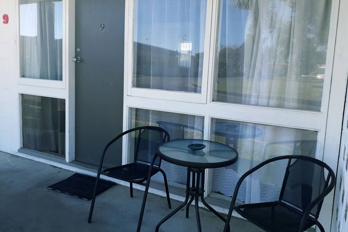 A room with a door marked '9', a glass door, a small round table with a chair, and a black chair.