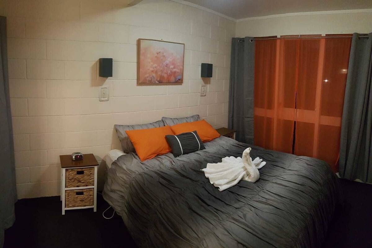 A hotel room with a bed, a nightstand, a painting on the wall, and a window with curtains.