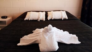 Una cama bien hecha con almohadas y una toalla blancos, un cabecero de madera oscura y dos lámparas de pared.