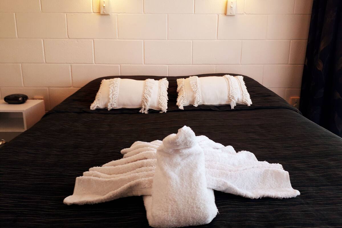 A neatly made bed with white pillows and a white towel, a dark wooden headboard, and two wall-mounted light fixtures.