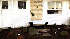 Una casa blanca con un banco de madera y un jardín con diversas plantas y piedras para pisar.
