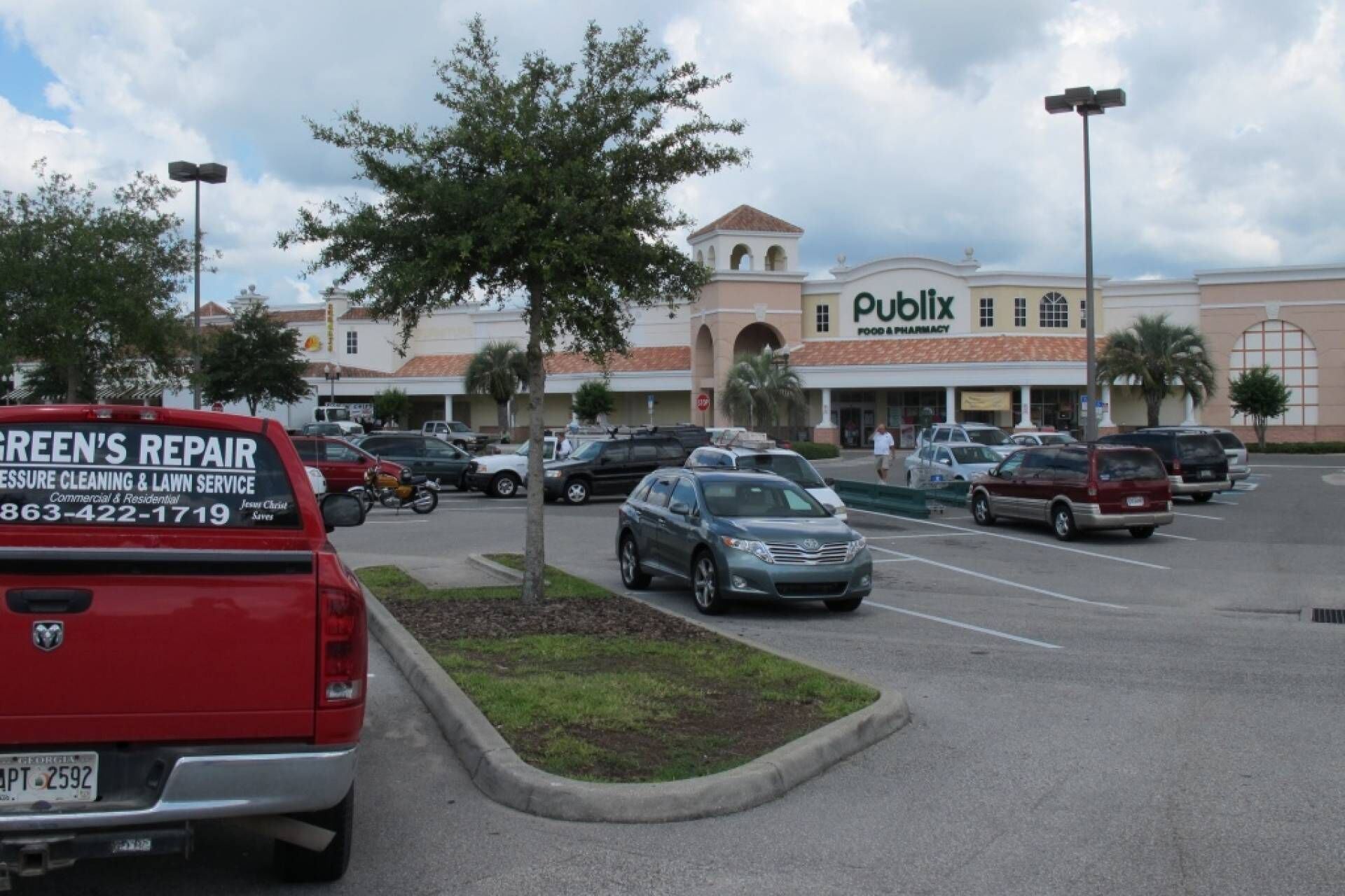 Un parking avec plusieurs voitures, un véhicule rouge portant une publicité commerciale, et un magasin Publix en arrière-plan.