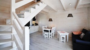 Een modern interieur met een trap naar een slaapkamer op een entresol, een eethoek met witte meubels, en een gezellige zithoek met een zwarte bank.