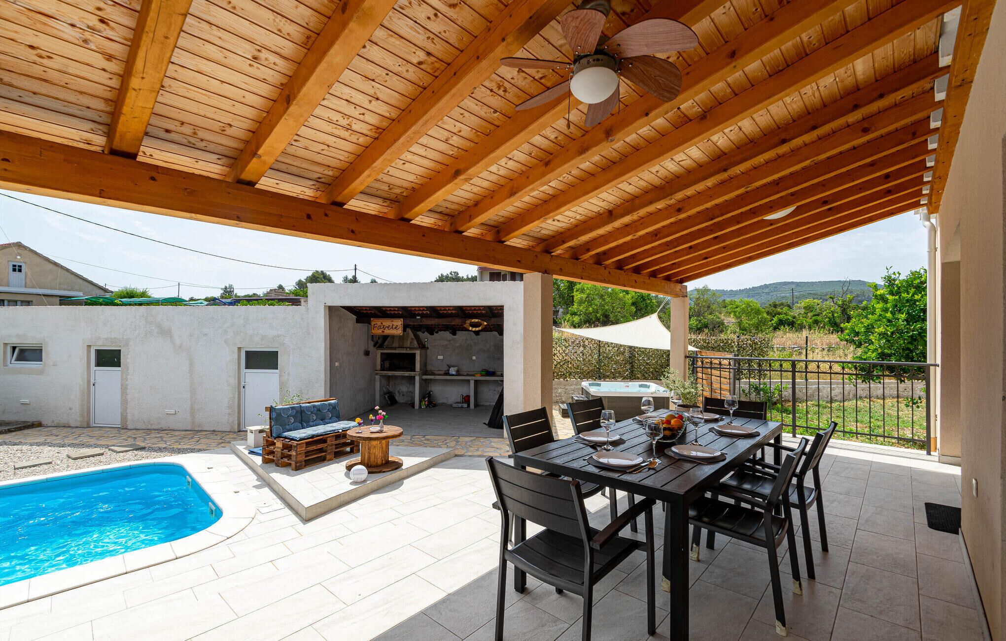 Ein überdachter Außenbereich mit Pool, Esstisch und Grill.