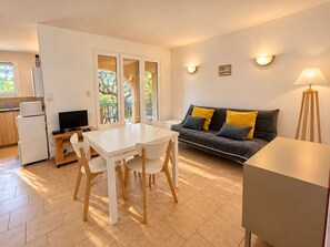 A compact living space with a dining area, a sofa with cushions, a lamp, and a television.